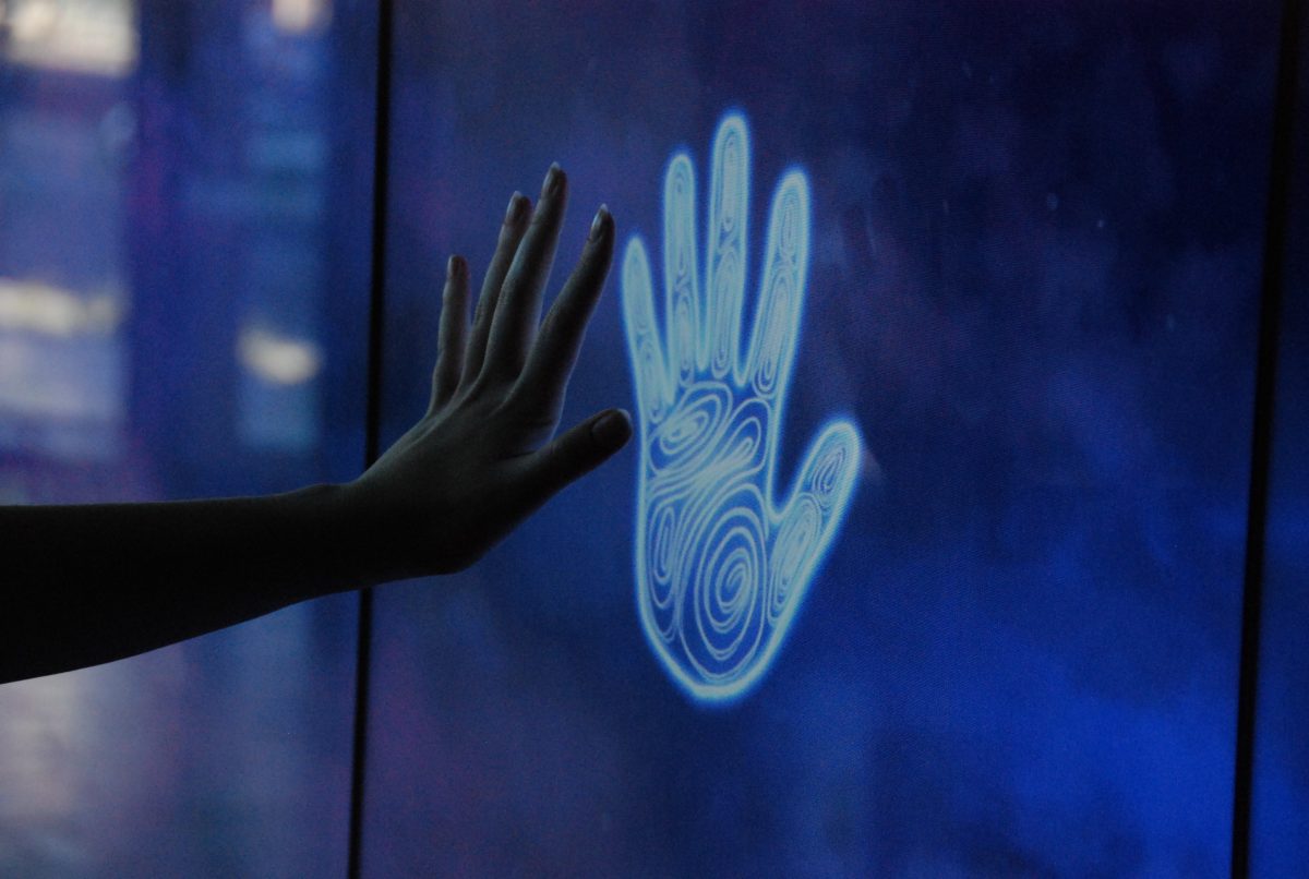 A hand reaching out to touch a glowing hand print on a digital screen