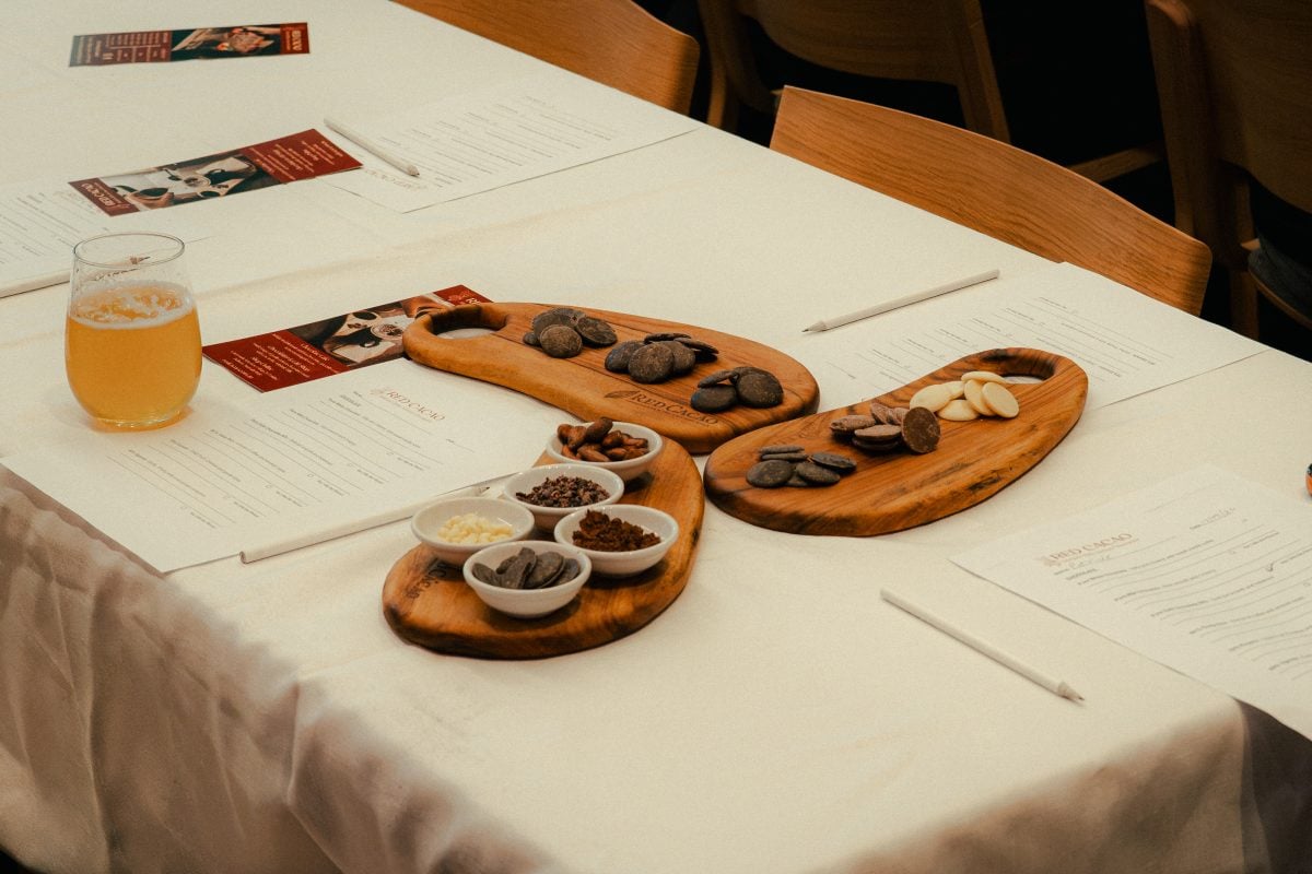 Three wooden platters are on a table, they are arranged like a fan and each have different stages of chocolate production display on them, including chocolate pastilles.