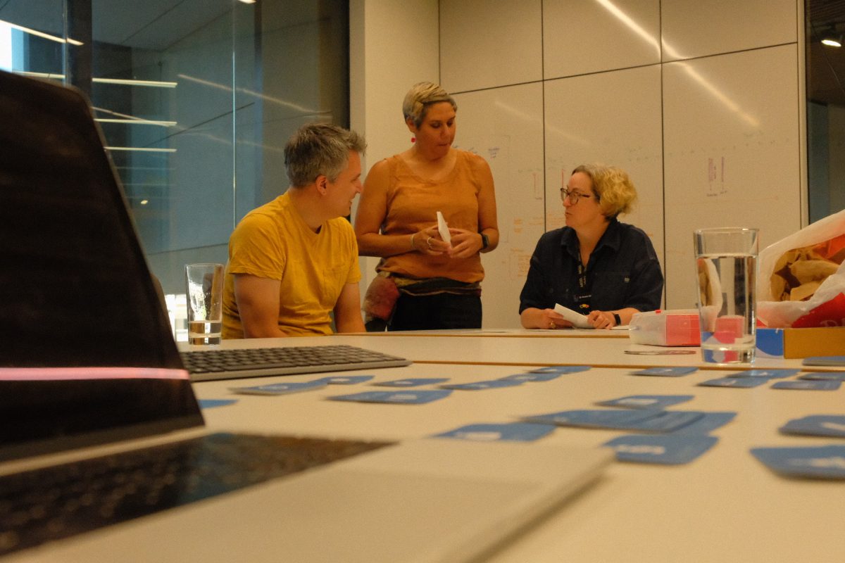 Mike, Jilda and Kristin pictured in discussion around a table covered in cards and post-it notes.