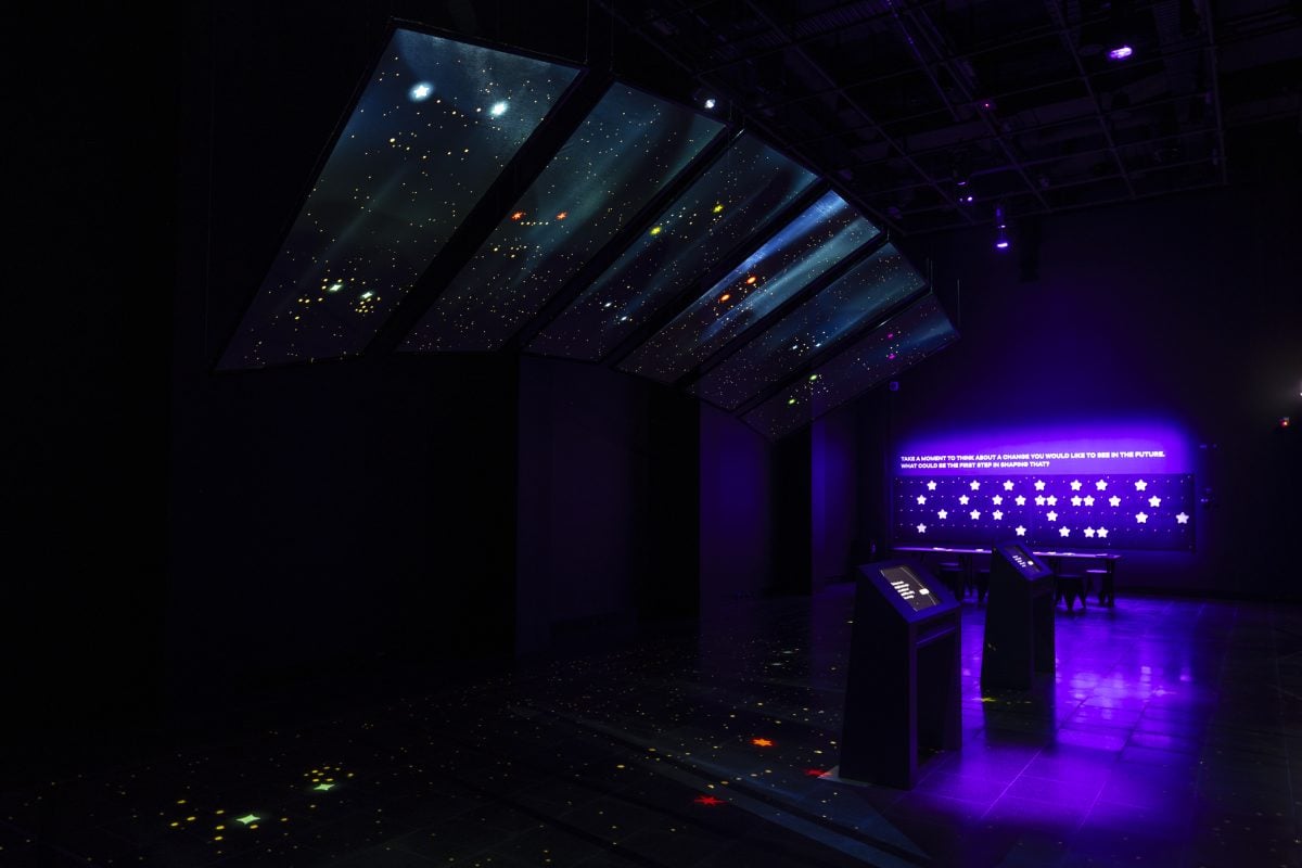 A long shot of a gallery space showing a celestial ceiling projection.