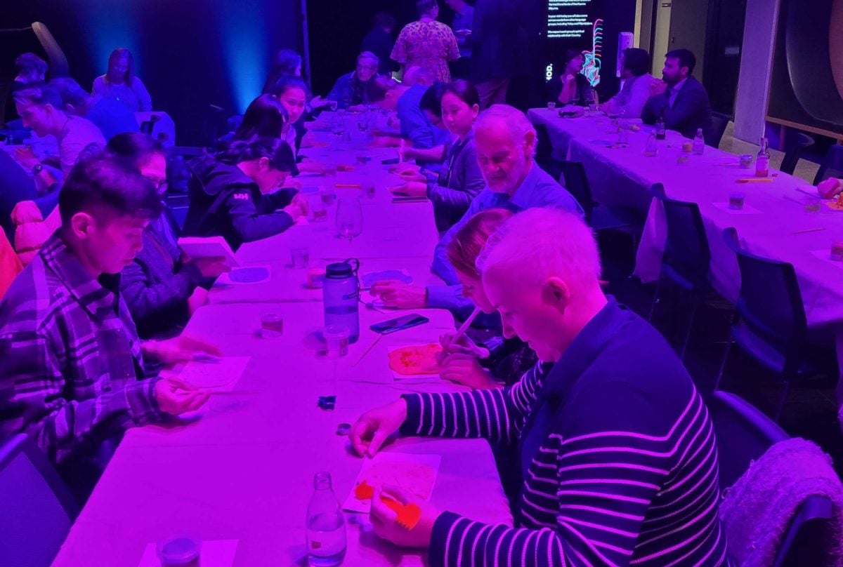 Two long rows of tables with people sitting and crafting with Play-Doh. The image is bathed in pink light.