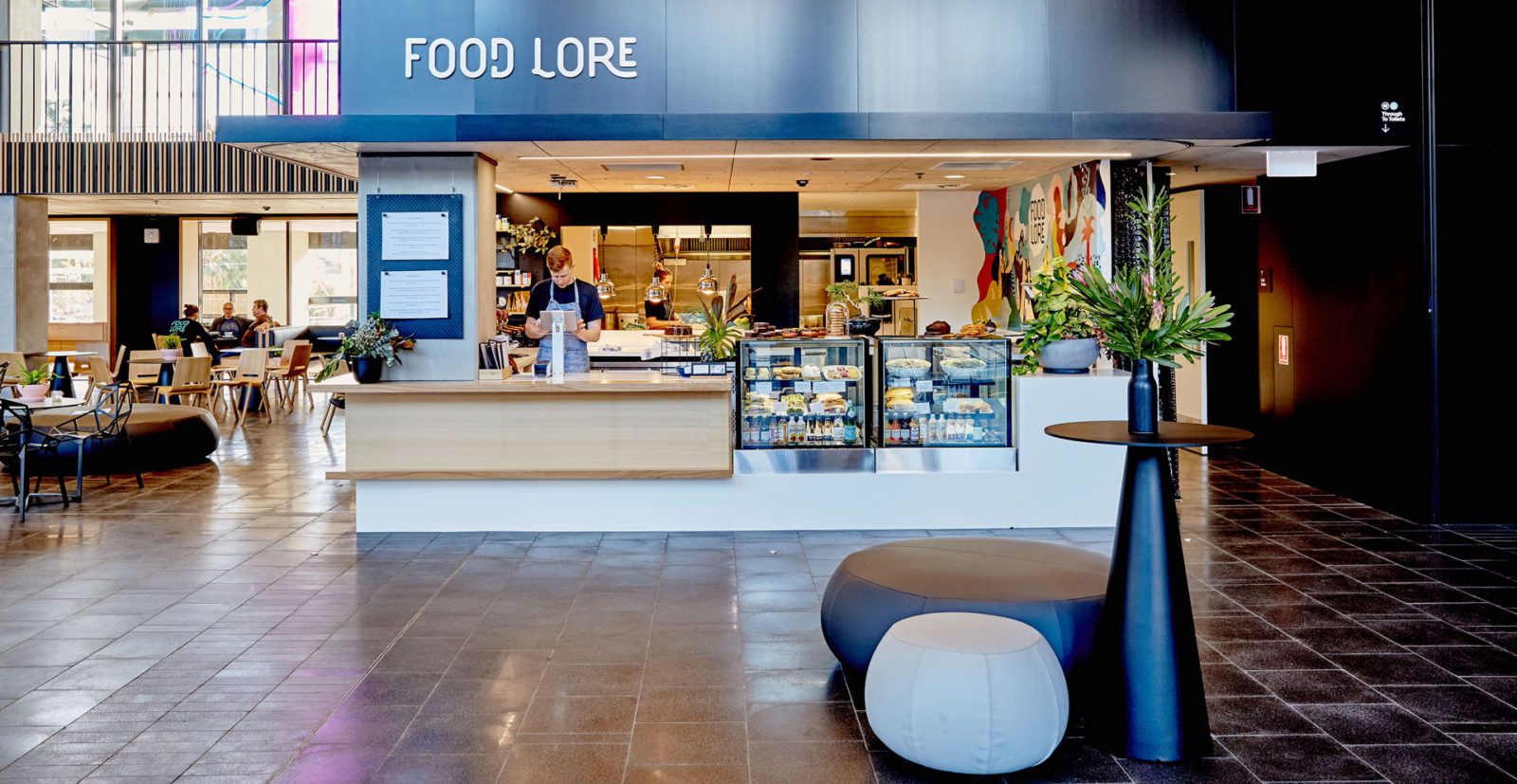 Food Lore café in the MOD. foyer - there is a staff member standing at the counter and fridges filled with cakes and sandwiches.