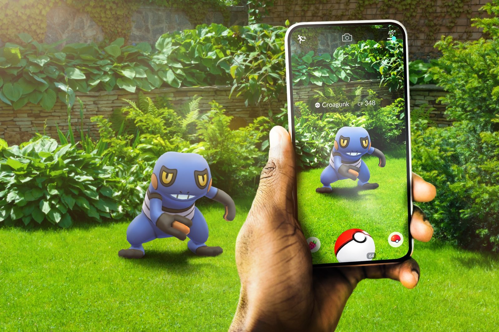 A hand holds out a smart phone with an image of a pokemon on it. The same pokemon is in the background on the grass.
